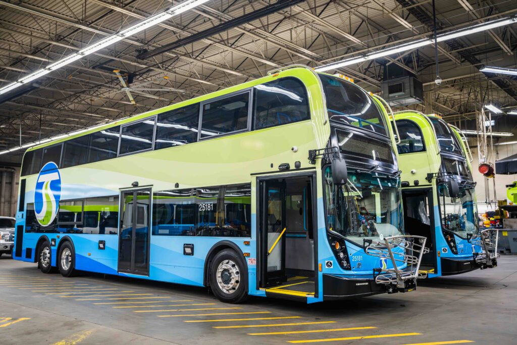 Two blue and green double-decker buses parked inside a large garage.