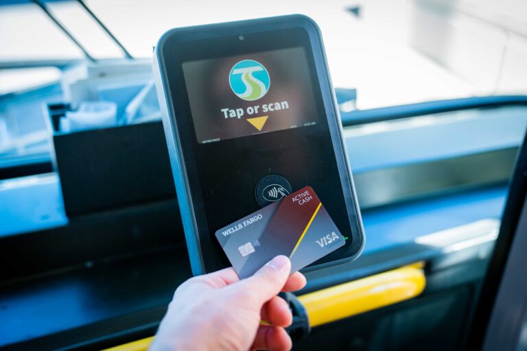 A person holds a Wells Fargo Visa card to a contactless payment terminal on an STA bus.