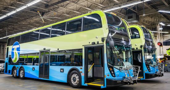 Two blue and green double-decker buses parked inside a large garage.