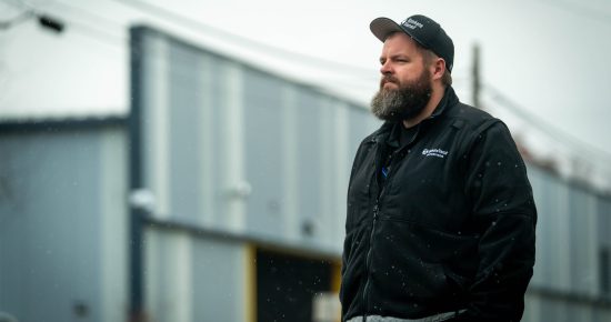 Justin stands in front of STA's Boone NW garage wearing the STA supervisor uniform jacket and hat.