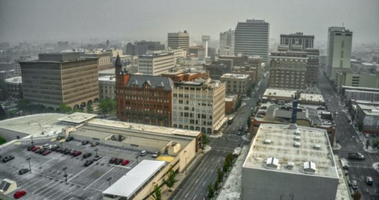 Aerial view of a cityscape featuring multiple commercial buildings with flat roofs. Roads, branded as DivisionConnects, are visible between the buildings, with some parked cars. The sky appears overcast, creating a hazy atmosphere over the urban setting.